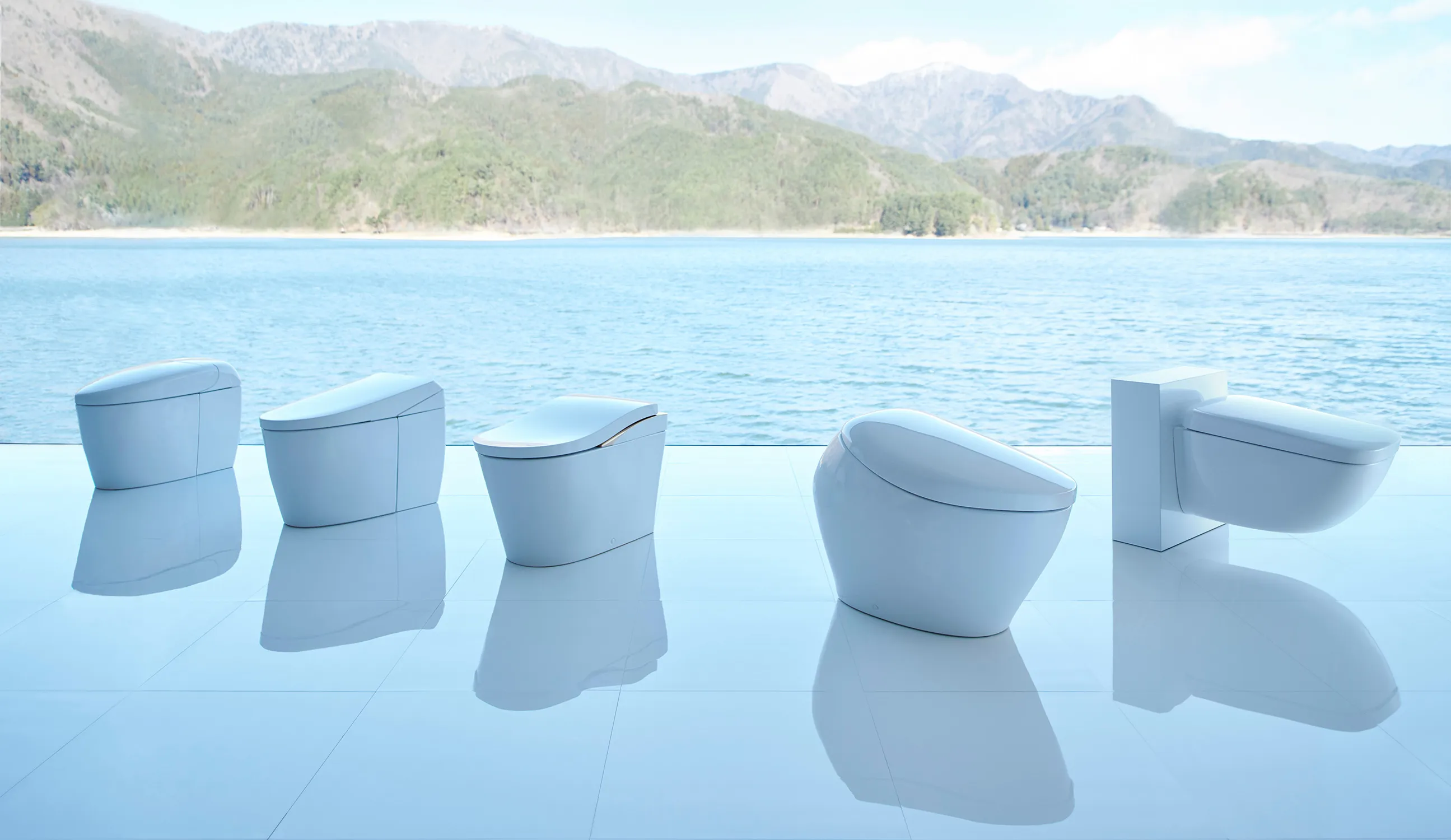 A row of NEOREST toilets is displayed on a glossy white floor with a stunning backdrop of a lake and mountains.