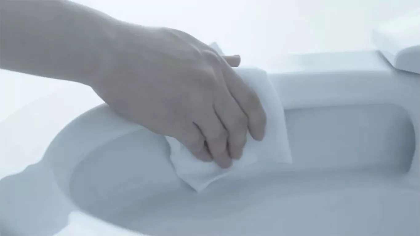 A hand wiping smooth rimless toilet bowl surface, demonstrating easy-to-clean design of TOTO rimless toilets with CEFIONTECT glaze.