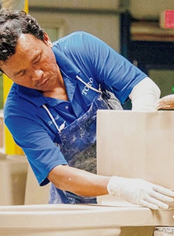 Photo of TOTO line assembly worker putting finishing touches on a freshly created ceramic toilet.