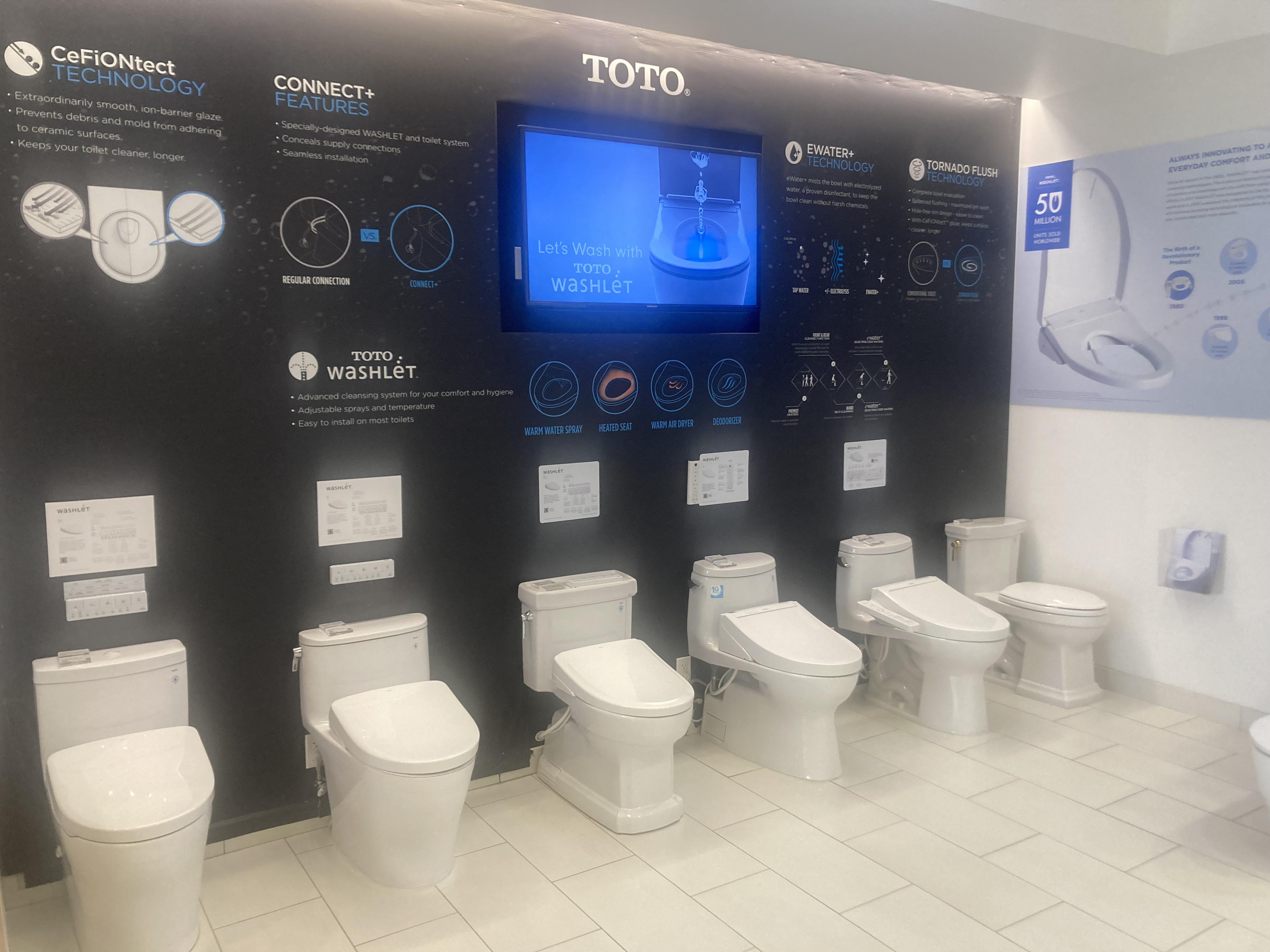 Toilets on display in front of wall with information and video screen