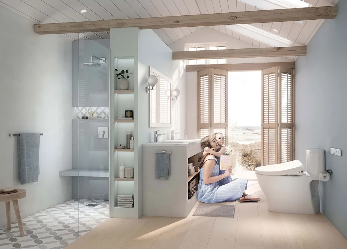 A mother and child sit in a bright, modern bathroom near a bidet toilet, with sunlight streaming through beachside windows.