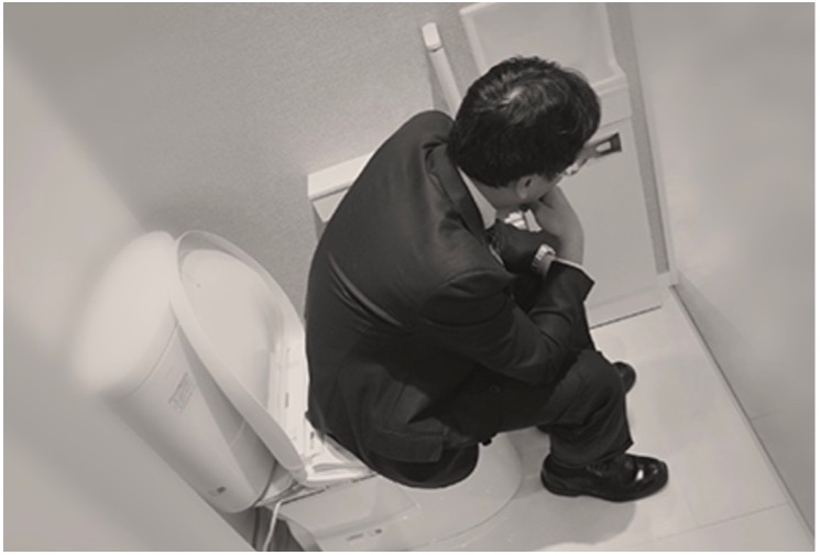 A TOTO employee dressed in a business suit sits on WASHLET prototype bidet seat simulating the product testing employees did during its development. 